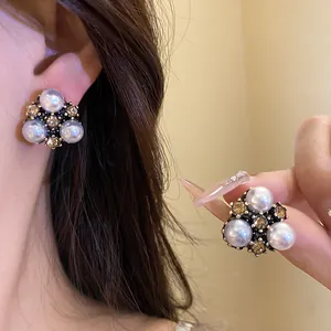 Dettaglio di orecchini di perle vintage con strass ambrati su orecchio e mano.
