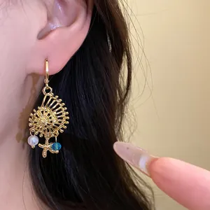 Detalle de pendientes de concha dorada con perla y dijes de estrella de mar
