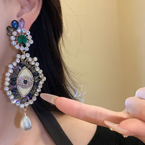 Close-up of vintage style eye motif earrings with crystals and pearl drop on ear