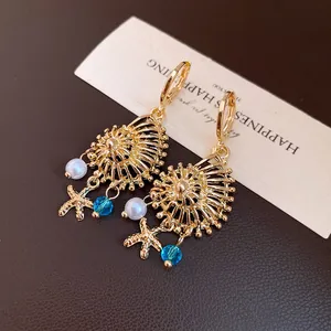 Primer plano de pendientes colgantes vintage de oro con concha, estrella de mar y perlas.