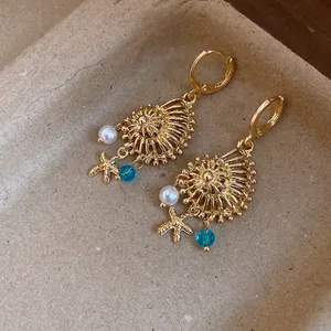Detalle de pendientes de aro dorados vintage con colgantes de concha, estrella y perla.
