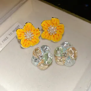 Dettaglio di orecchini a lobo a fiore in smalto e metallo con zirconi brillanti.