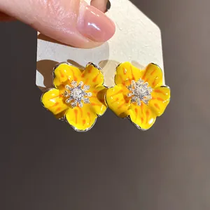 Dettaglio di orecchini a fiore in smalto giallo con zirconi e perle al centro