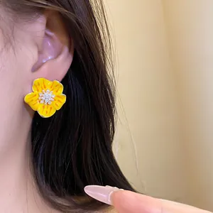 Primo piano di orecchino a forma di fiore in smalto giallo con centro di zirconi.