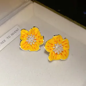 Dettaglio macro di orecchini a lobo a fiore in smalto giallo con zirconi e perle