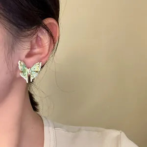 Close-up of elegant green and white enamel butterfly earrings worn on an ear