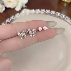 Elegant set of silver-tone hollow butterfly and small pearl stud earrings on a hand