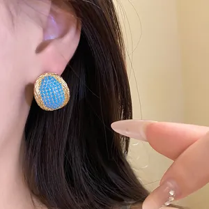 Close-up of vintage oval gold-toned stud earrings with blue stones on a model's ear.