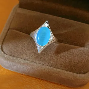Close-up of a silver-toned starburst ring with a blue cat eye stone in a brown box