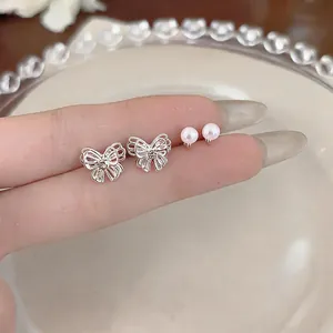 Macro detail of delicate silver butterfly and pearl stud earrings shown on a finger
