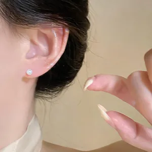 Close-up view of a minimalist white pearl stud earring worn on a female ear lobe.