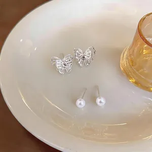 Detailed view of silver butterfly and pearl stud earrings on a white ceramic plate
