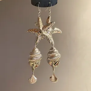 Close-up of metallic silver starfish and conch shell drop earrings for beach style