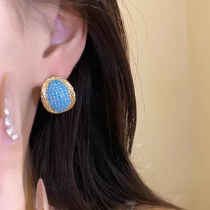 Close-up of vintage gold oval stud earrings with turquoise pavé stones on ear.