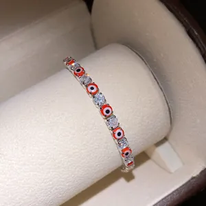 Macro detail of silver-tone tennis bracelet with red evil eye charms and CZ stones.