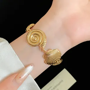 Detailed view of vintage style gold shell and conch bracelet worn on a woman's wrist