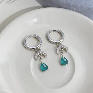 Close-up of zircon moon earrings with teal teardrop gemstone pendants for women.