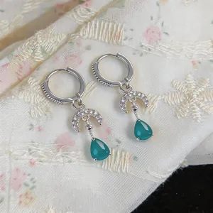 Detailed view of silver-toned hoop earrings with zircon moon and green teardrop stone.