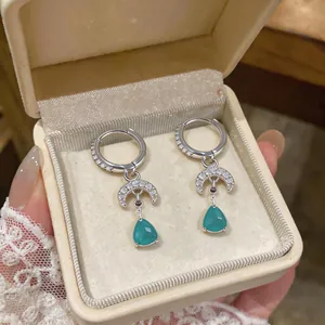 Detail view of silver hoop earrings with crescent moon and green teardrop pendants.