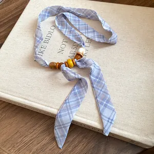 Close-up detail of blue plaid ribbon necklace with colorful polished beads on a book.