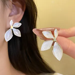 Close-up of white enamel flower stud earrings with a vintage refined gold-plated finish.