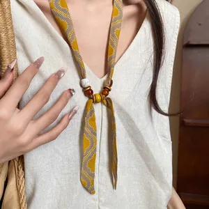 Close-up of a yellow patterned fabric necklace with wooden beads on a linen top
