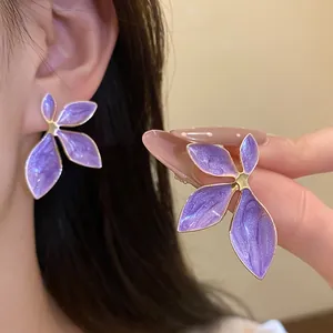 Close-up detail of purple oil-drop flower stud earrings with gold-toned metal edges