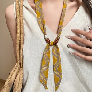 Detailed shot of a yellow wavy print fabric necklace with beads worn by a model