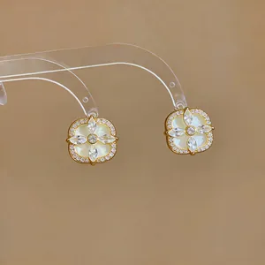 Gros plan de boucles d'oreilles fleurs dorées avec zircons sur un support transparent.