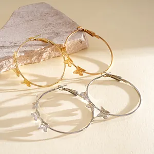 Close-up detail of gold and silver butterfly hoop earrings on a textured stone slab.
