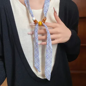 Detailed view of a stylish blue plaid beaded scarf necklace worn with a black cardigan.