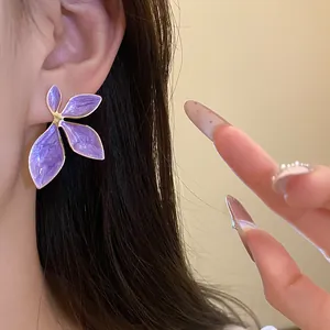 Close-up detail of a purple oil-drop flower earring with gold edges on model's ear.