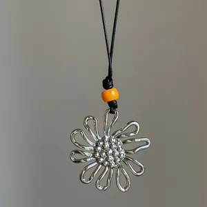 Detail shot of a silver pleated flower pendant with an orange bead on a black cord.