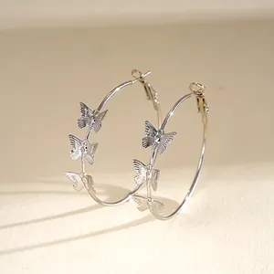 Detailed side view of silver hoop earrings featuring delicate butterfly charms on a cream base