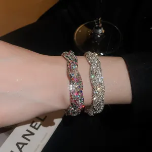 Detailaufnahme von geflochtenen Vintage-Strassarmbändern am Handgelenk bei wenig Licht.