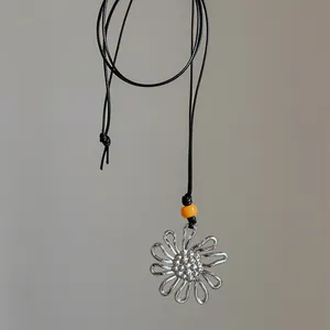 Detail of a silver pleated flower pendant necklace with an orange bead and black cord.