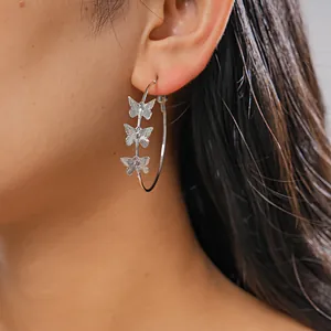 Close-up of silver-tone hoop earrings with three butterfly charms on model's ear
