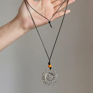Close-up of a silver flower pendant necklace with a black cord and orange bead.