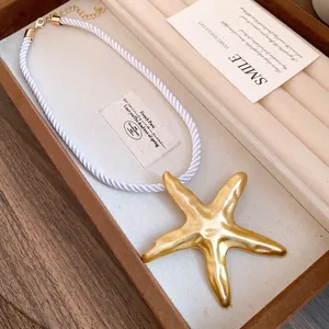 Close-up detail of a vintage golden starfish pendant on a white twisted rope cord necklace