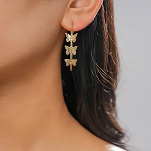 Close-up of gold hoop earrings featuring three delicate butterfly charms on a model.