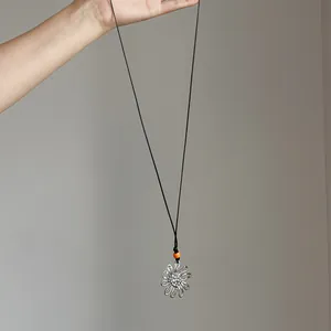 Close-up of a large silver hollow flower pendant on a long black cord necklace with orange bead