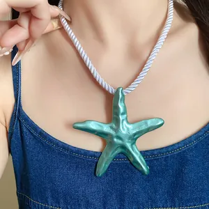 Detail view of a turquoise starfish pendant necklace on a white silk rope chain