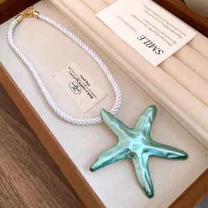Close-up of a teal starfish pendant with metallic finish on a white twisted silk cord