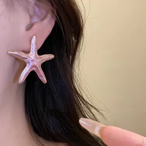 Detailed view of a pink metallic starfish stud earring worn on an ear for vacation style