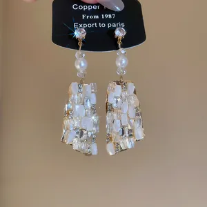 Detalle de los pendientes colgantes de cristal de lujo con pedrería y perlas blancas.
