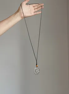 Detail view of vintage pleated flower pendant necklace with orange bead on black cord