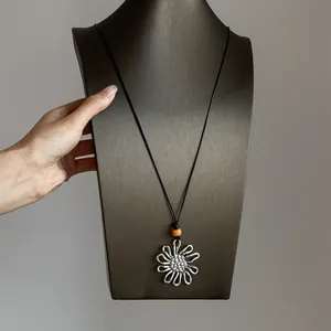 Retro silver flower pendant necklace with orange bead on a minimalist black cord.
