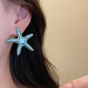 Detailed close-up of a large blue starfish earring being worn for a beach vacation style.