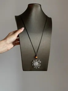 Detailed view of a retro metallic flower pendant necklace with a small orange bead.