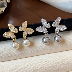 Macro detail of elegant butterfly pearl drop earrings in gold and silver finishes.